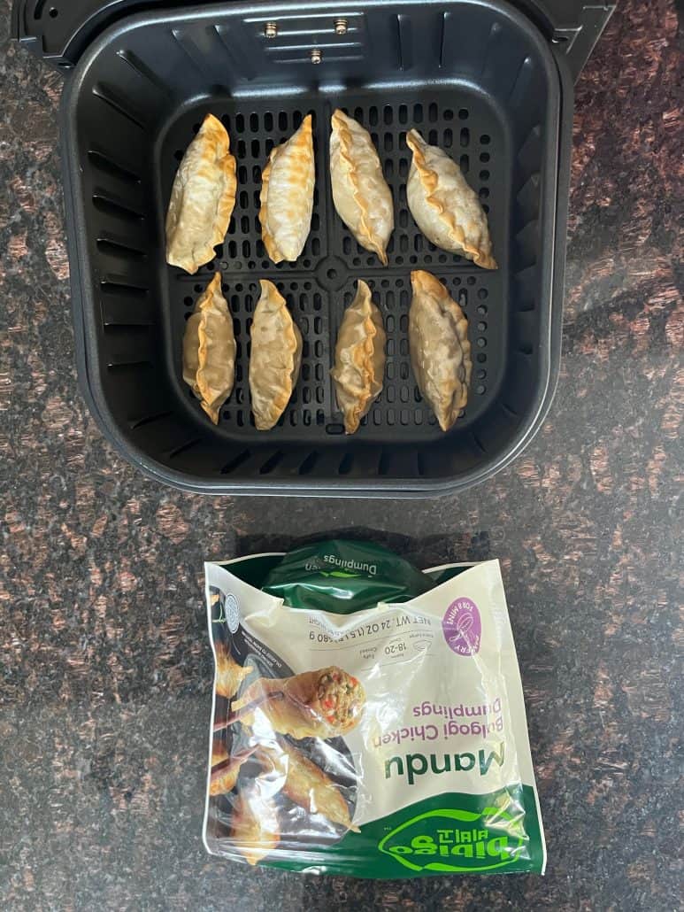 Air fryer basket with Bibigo Mandu dumplings next to the packaging.