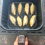 Crispy golden-brown frozen dumplings cooked in an air fryer basket, ready to serve as a quick and delicious snack.