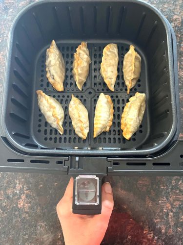 Crispy golden-brown frozen dumplings cooked in an air fryer basket, ready to serve as a quick and delicious snack.