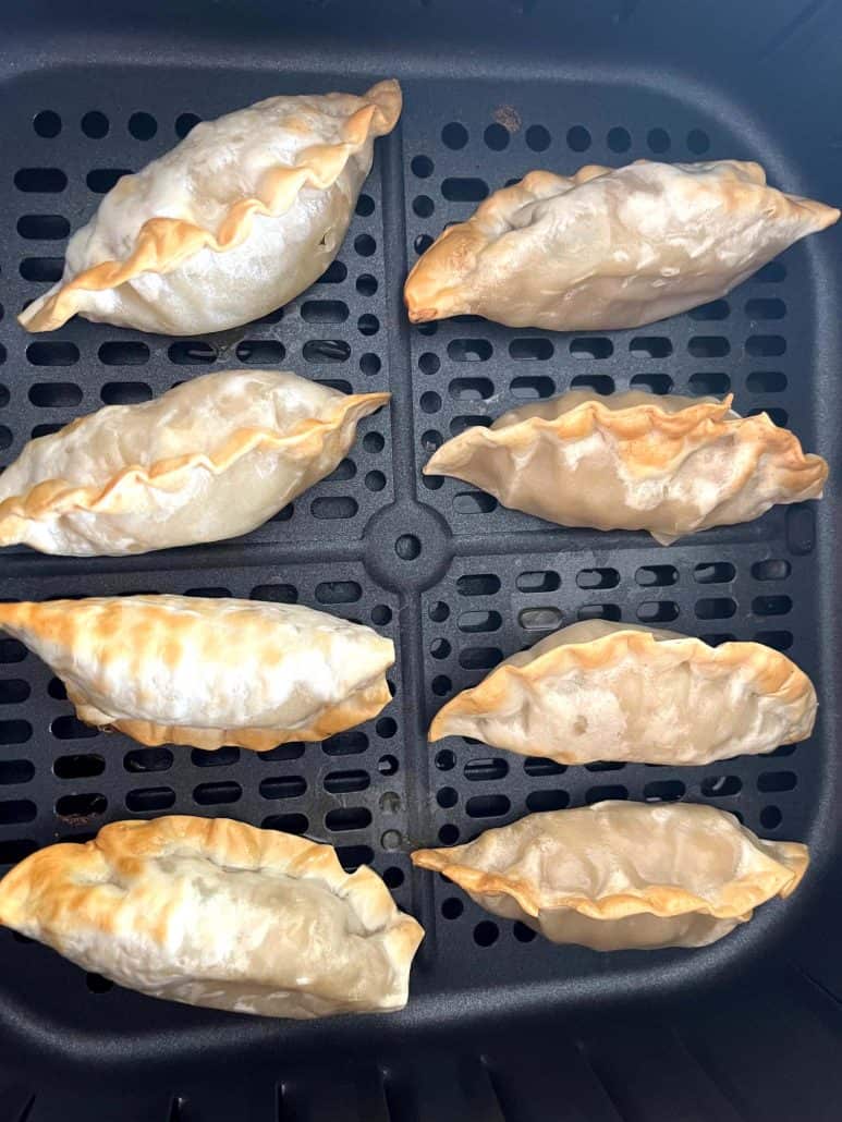 Close-up of eight crispy Mandu dumplings in an air fryer basket, showing their golden-brown texture after cooking.