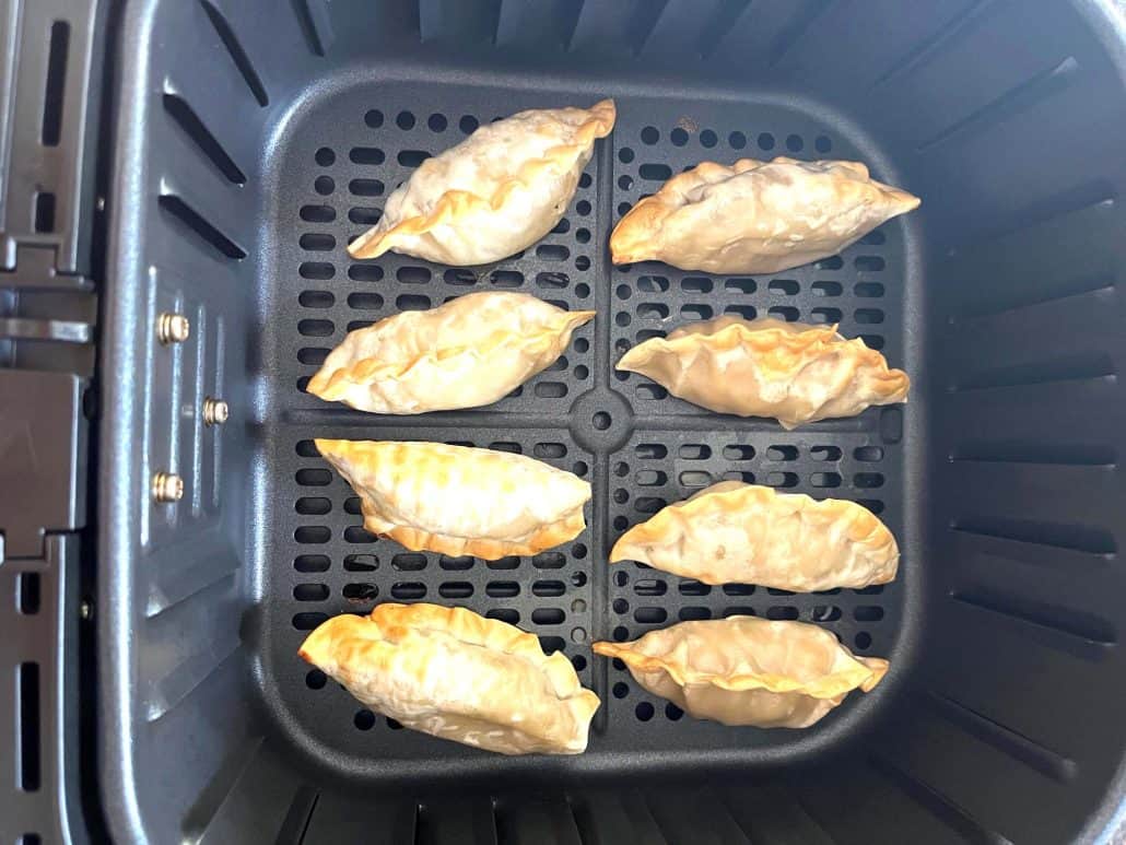 Evenly browned air-fried Mandu dumplings, in a single layer inside an air fryer basket.