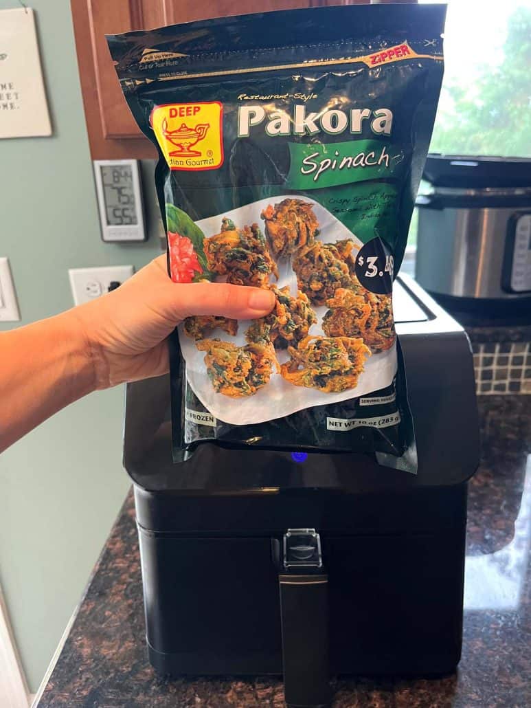 Holding a package of frozen spinach pakoras in front of the air fryer, ready to begin cooking.