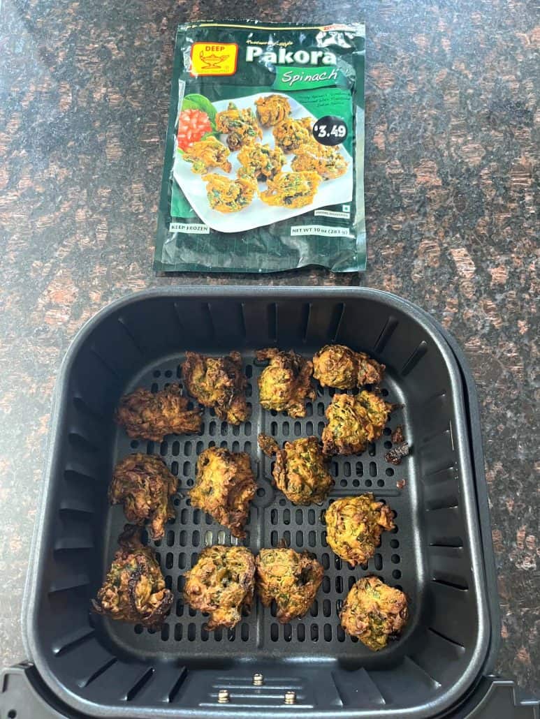 Air fryer basket filled with freshly cooked, golden pakoras beside the frozen pakoras package.