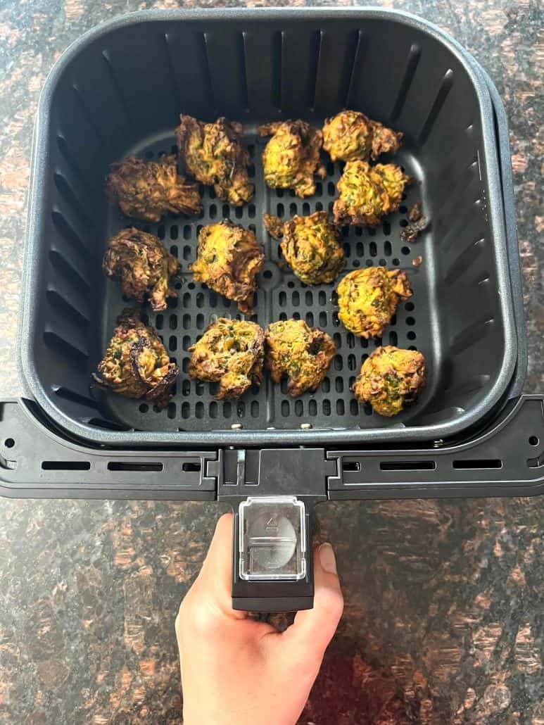 Air fryer basket filled with golden, crispy frozen pakoras after cooking.