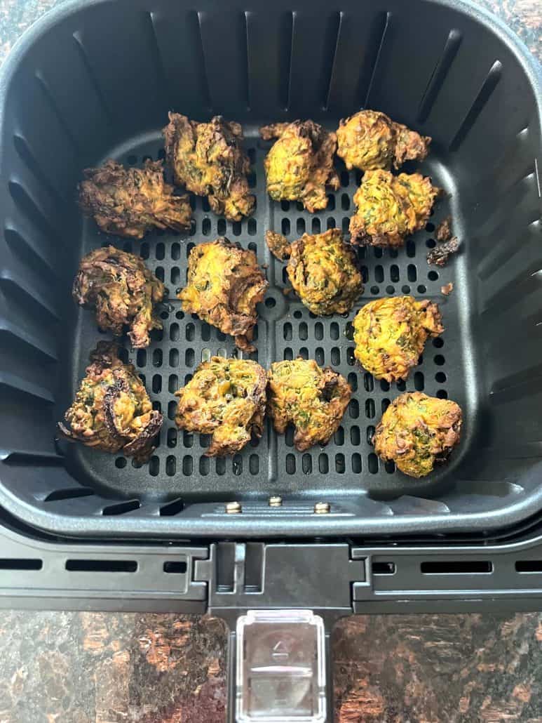 Golden pakoras in the air fryer basket, showing the even browning and perfect texture.