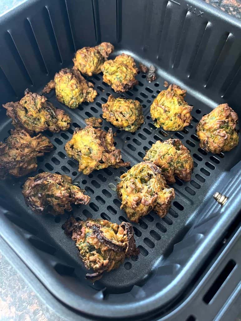 Angled view of crisp, delicious pakoras in the air fryer basket.