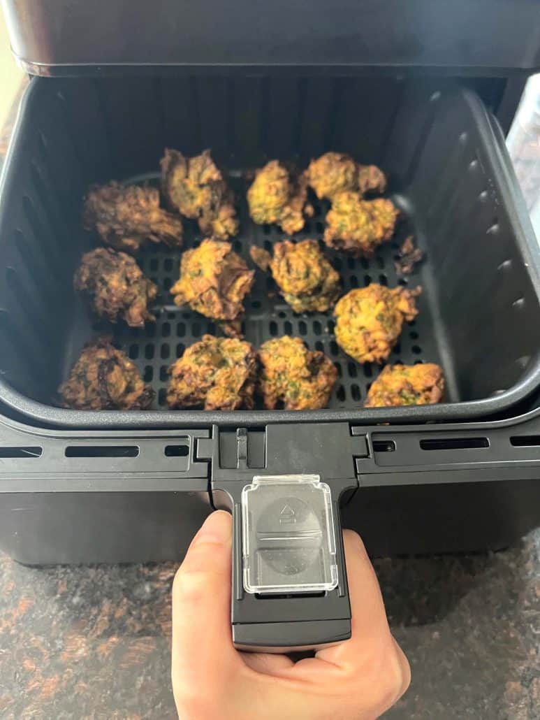 Hand holding the air fryer basket filled with freshly cooked, crispy pakoras, ready to serve .