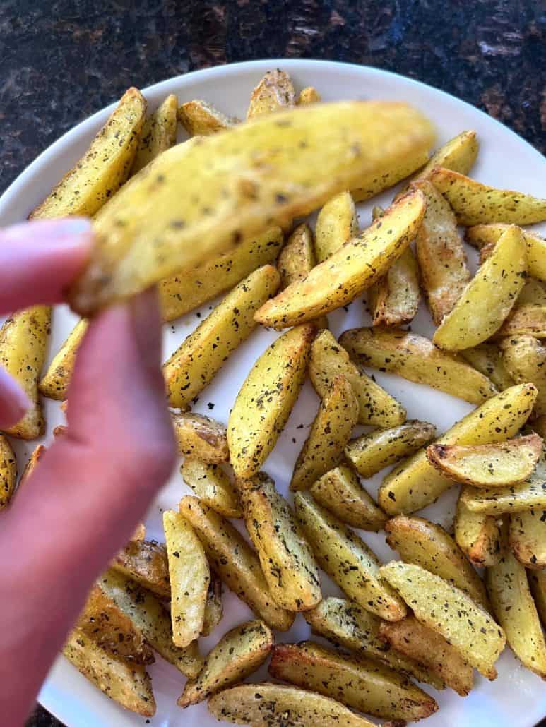 Close-up hand of Melanie Mendelson from melaniecooks.com holding a seasoned air-fried potato wedge, ready to enjoy.