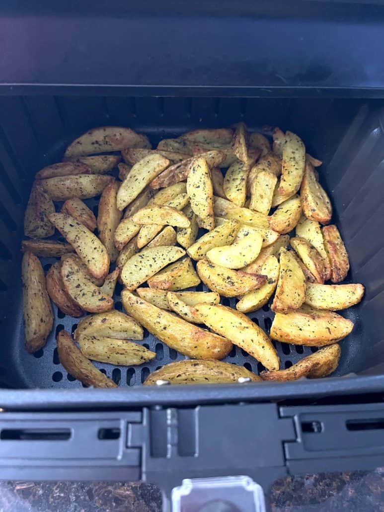 Close-up of crispy golden, seasoned potato wedges in an air fryer basket.