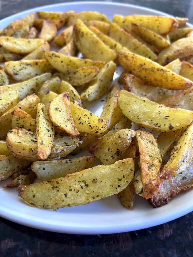 Seasoned crispy air-fried potato wedges, on a white plate, highlighting their golden-brown texture.