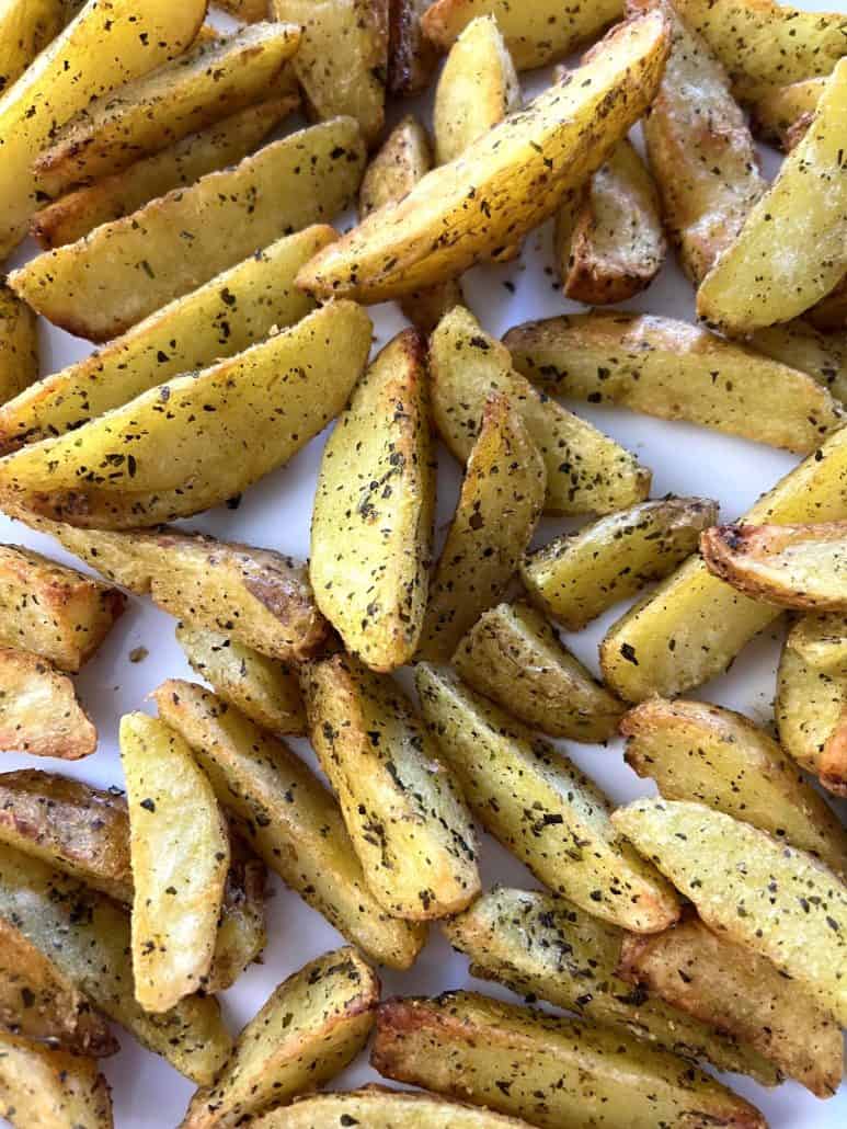 Another angle of golden, seasoned air-fried potato wedges spread on a white plate.