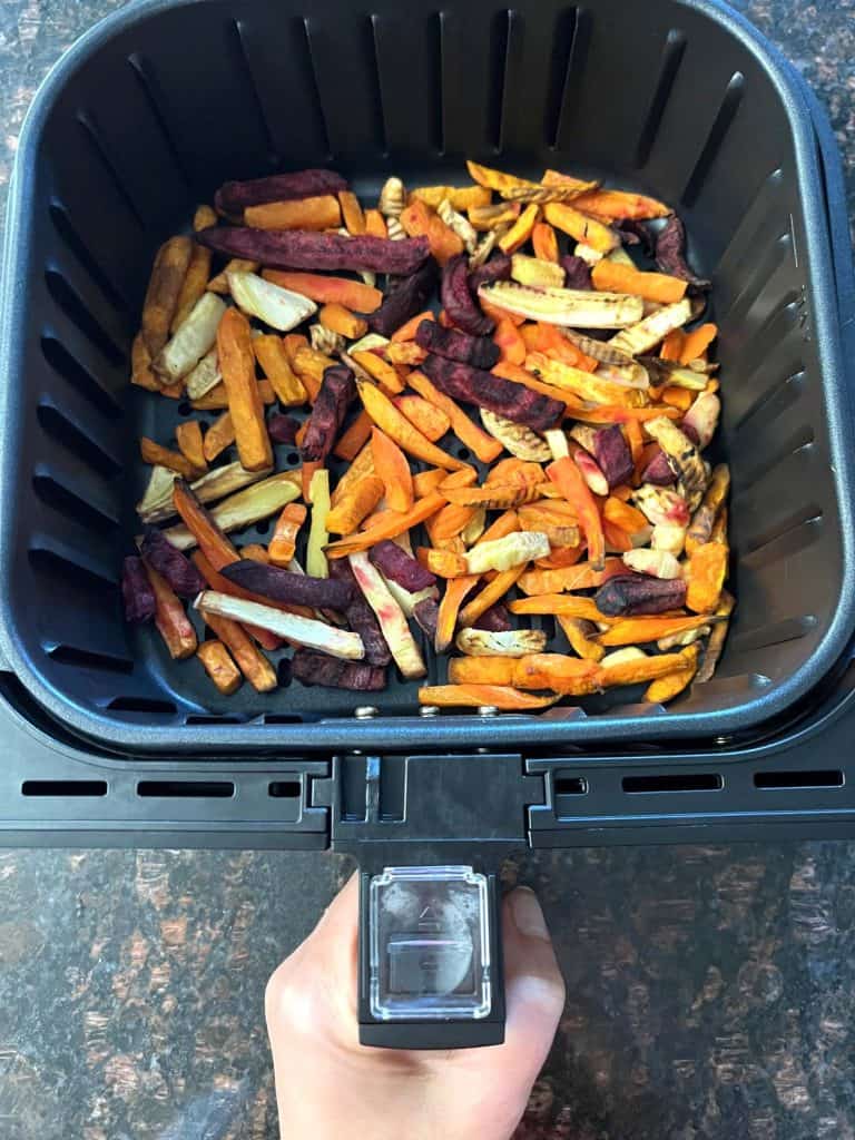 Air fryer basket filled with colorful root vegetable fries, including sweet potatoes, carrots, beets, and parsnips, ready for cooking as a healthy alternative to regular fries.