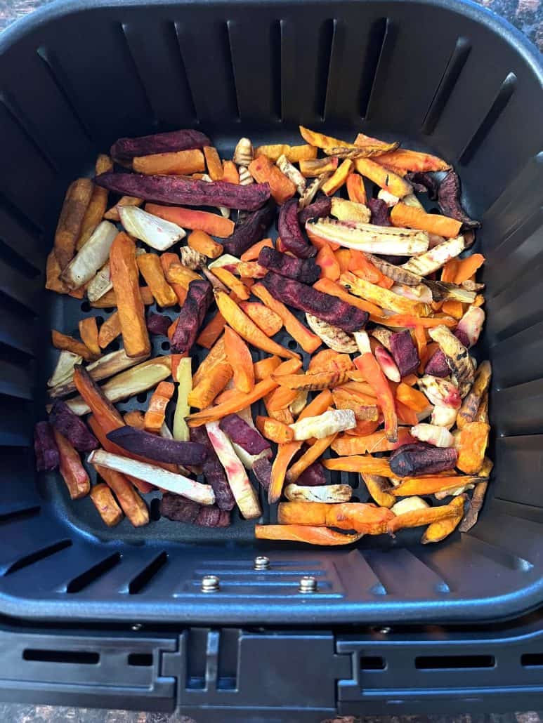 Air fryer basket filled with a colorful mix of frozen root vegetable fries, including sweet potatoes, carrots, beets, and parsnips.