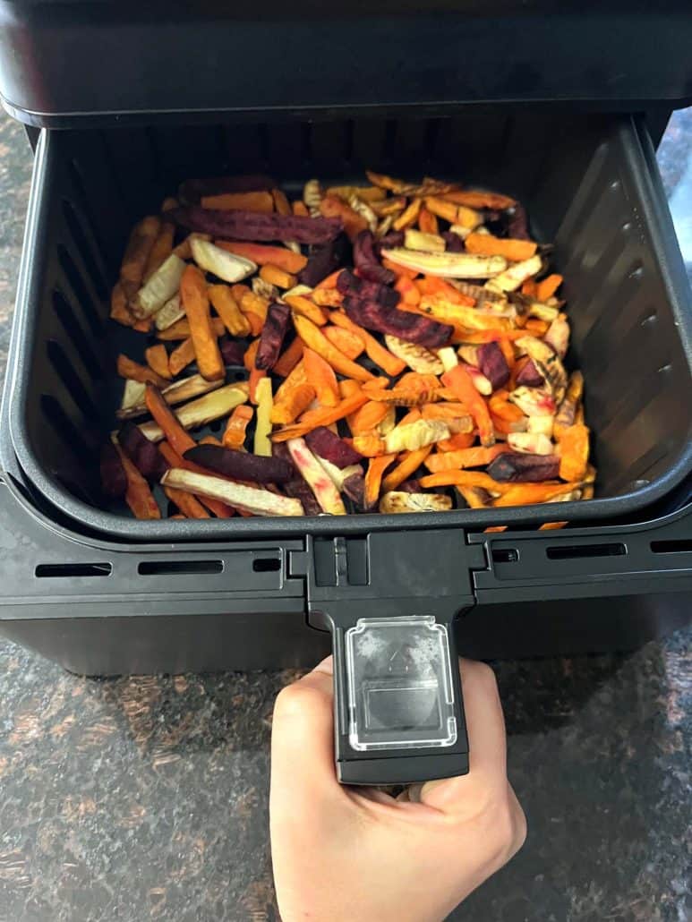 Air fryer basket filled with colorful root vegetable fries, including sweet potatoes, carrots, beets, and parsnips.