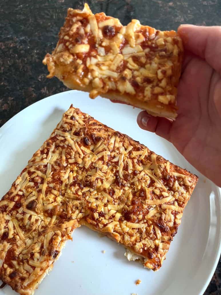 Holding a slice of air-fried Totino's Party Pizza, showing melted cheese and a crispy crust.