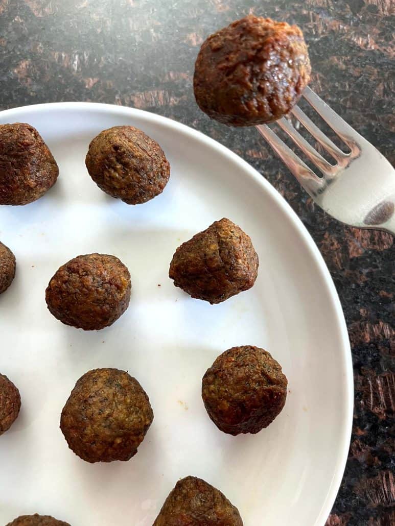 Fork holding a golden-brown air-fried Impossible Meatball above a plate.