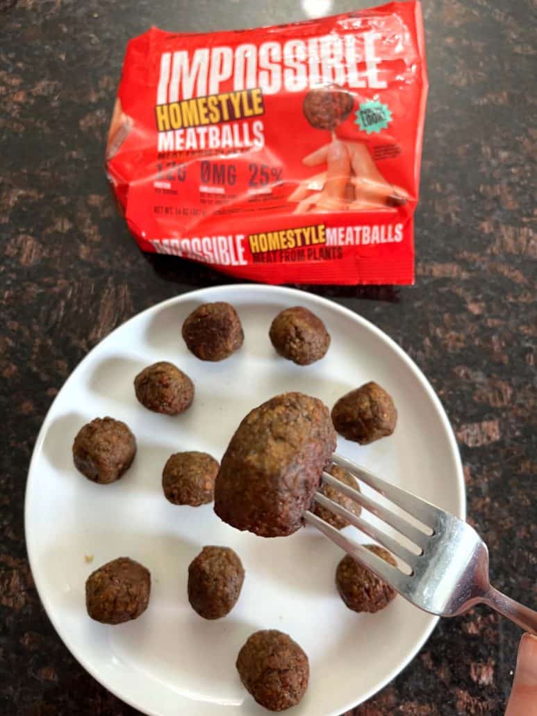 Holding a crispy air-fried Impossible Meatball above a plate, with the packaging in the background.