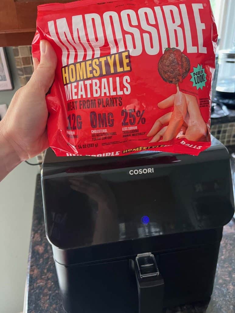 A package of Impossible Homestyle Meatballs above an air fryer, ready for quick and easy cooking of a vegan meal.