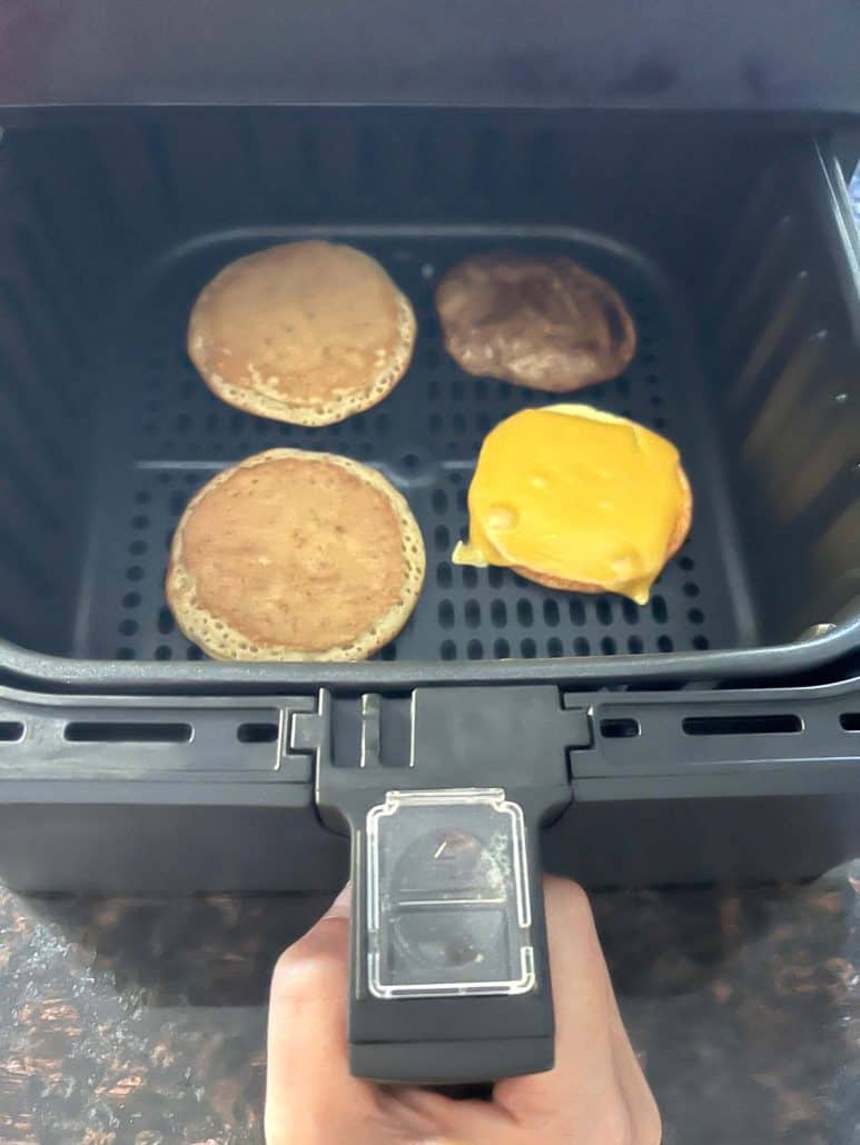 Air fryer basket with Jimmy Dean Maple Griddle Cake sandwich, including pancakes, sausage patty, and egg with melted cheese, showing the process of air frying breakfast sandwiches.