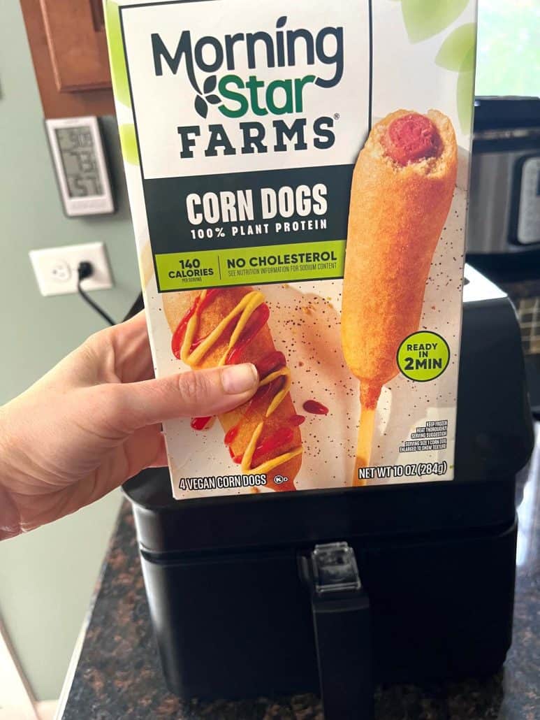 Holding a box of MorningStar Farms vegan corn dogs in front of an air fryer, ready for a quick cooking demonstration.