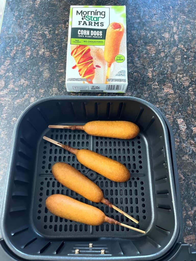 Vegan corn dogs in an air fryer basket with the MorningStar Farms corn dog package in the background.