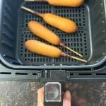 Four vegan corn dogs arranged in a single layer inside an air fryer basket.