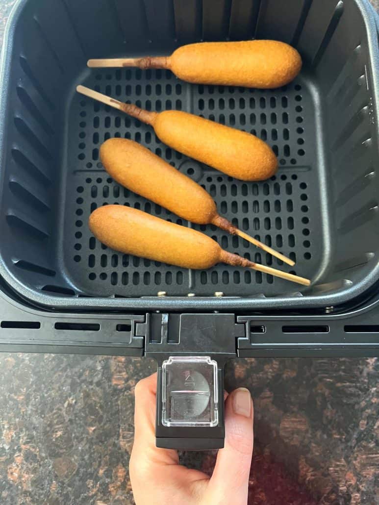 Four vegan corn dogs arranged in a single layer inside an air fryer basket.