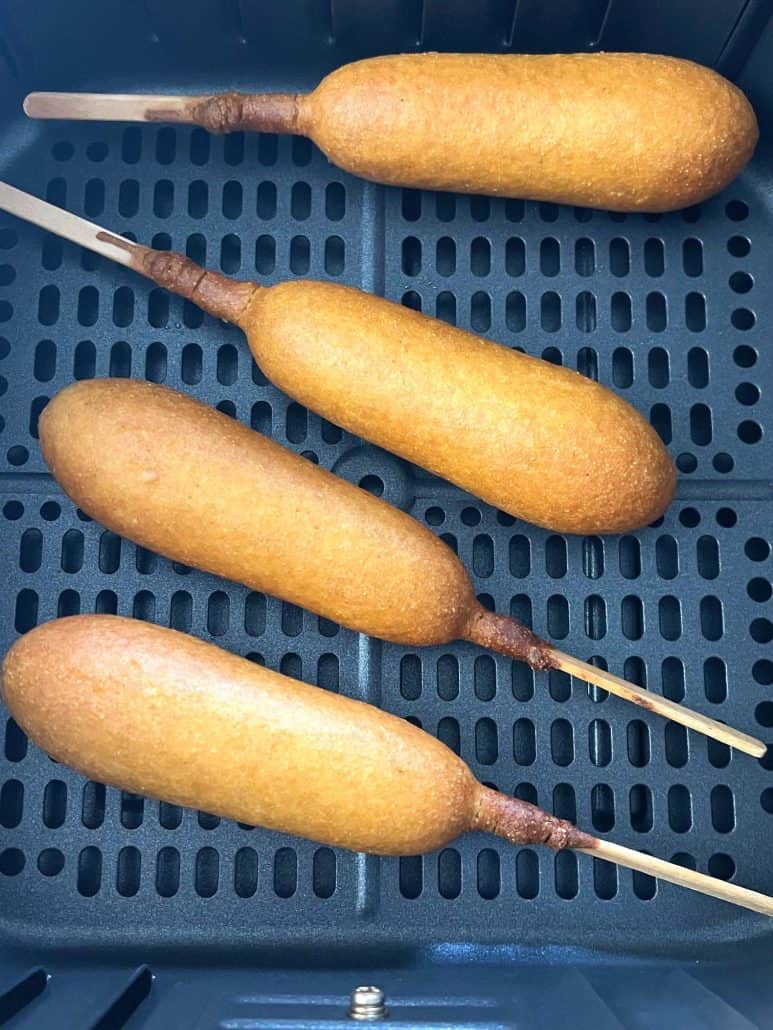 Close-up of four vegan corn dogs in an air fryer basket, cooked to a crispy golden finish.