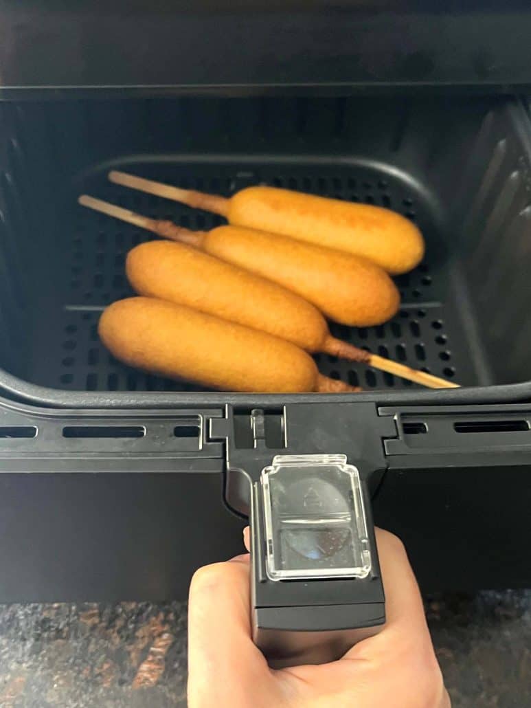 Air fryer basket with four freshly cooked vegan corn dogs. 