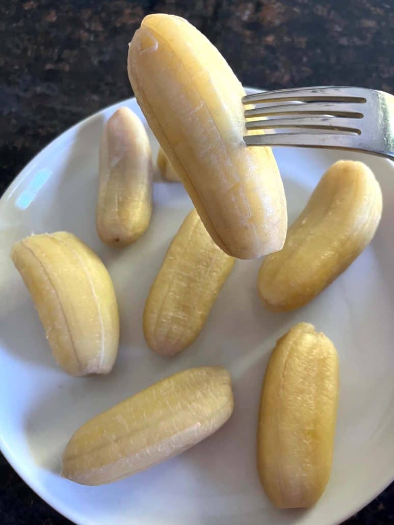 Fork holding a boiled Saba banana above a plate.