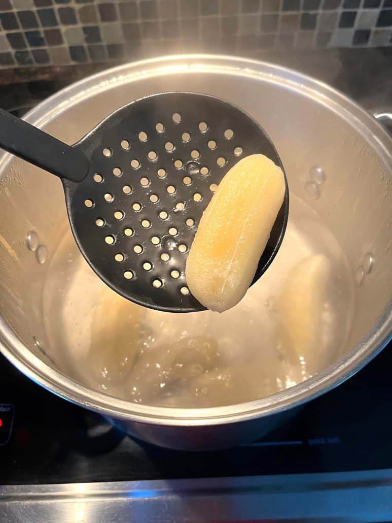 A slotted spoon lifting a boiled Saba banana from the pot.