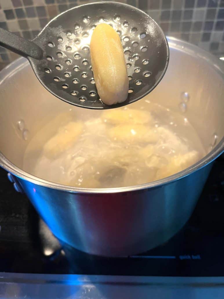 A slotted spoon showcasing a boiled Saba banana above a pot.