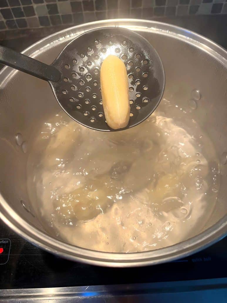 Slotted spoon lifting a boiled Saba banana, highlighting the final stage of the cooking process.