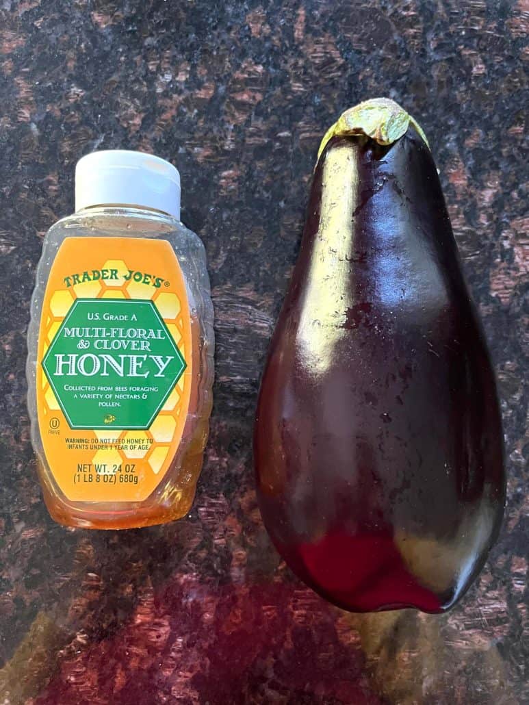 A fresh eggplant placed next to a bottle of honey on a kitchen countertop.