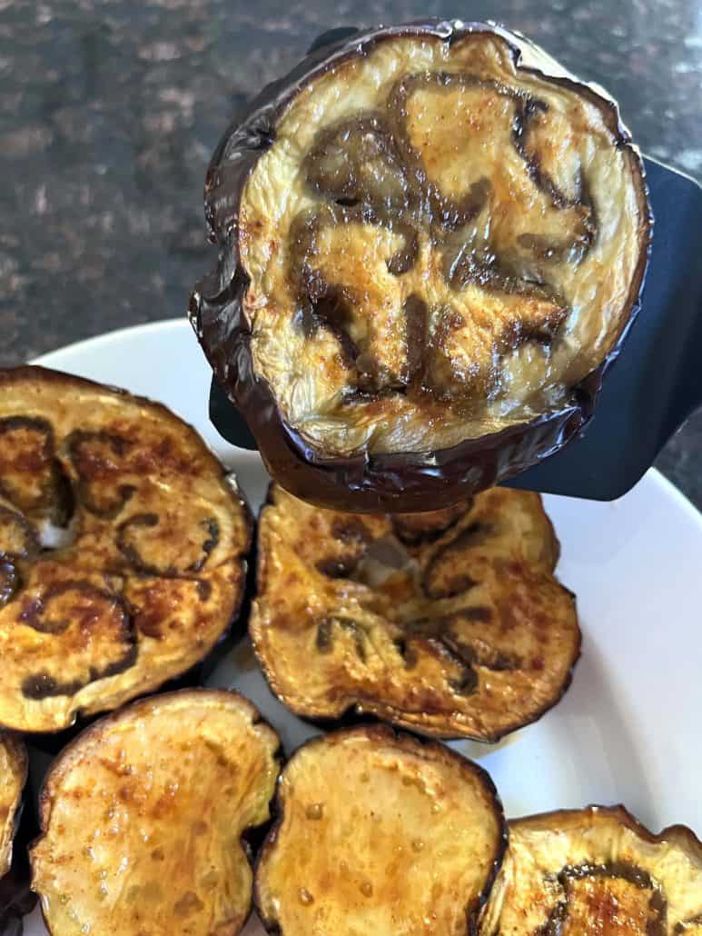 A close-up of a roasted eggplant slice held by a spatula.