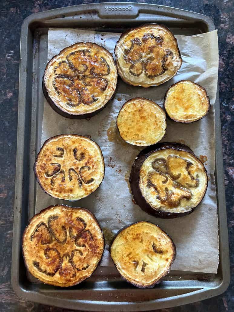 Roasted eggplant slices on a parchment-lined baking sheet, freshly taken out of the oven.