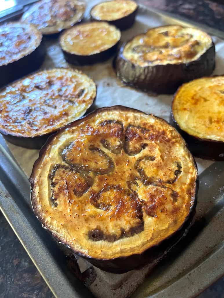 Close-up of perfectly roasted eggplant slices on a baking sheet.