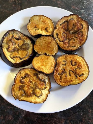 Golden-brown roasted eggplant slices served on a white plate.