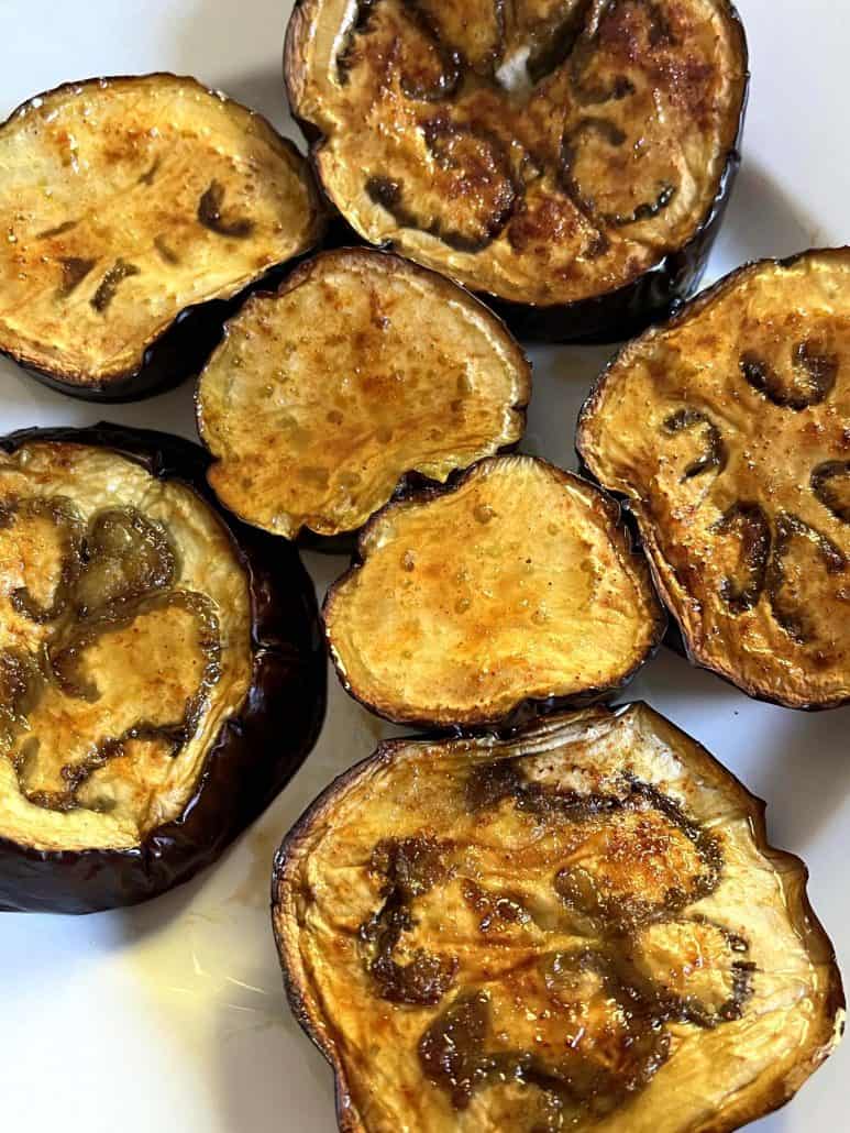 Roasted eggplant slices with golden-brown tops arranged on a white plate.