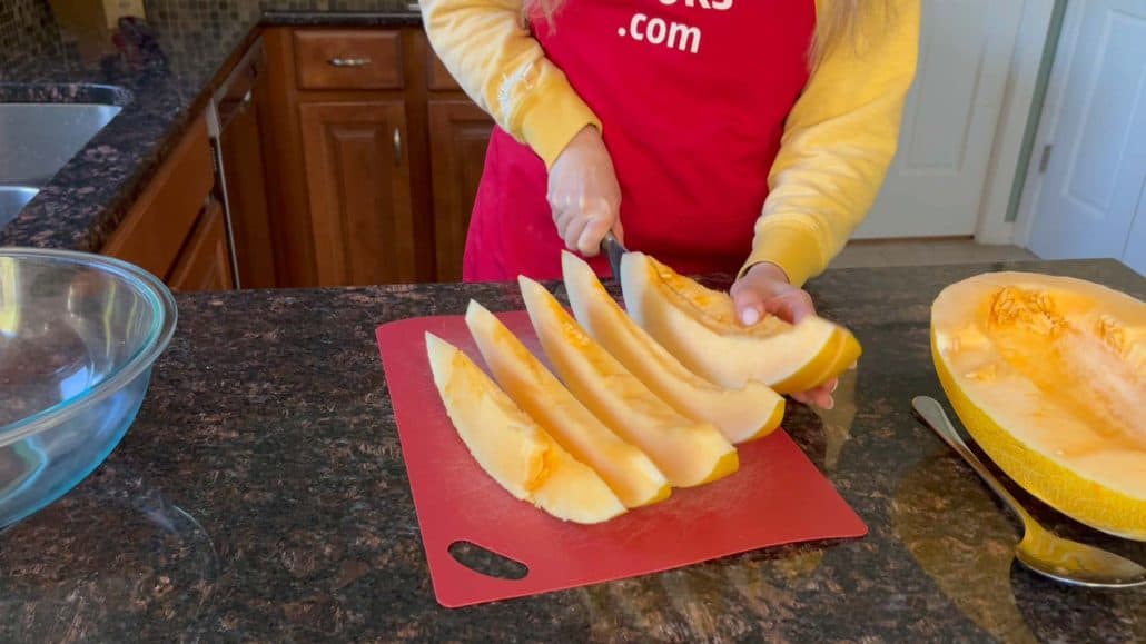 Melanie is cutting the Hami melon into pieces using knife and cutting board.