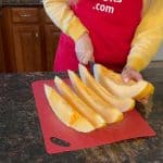 Melanie is cutting the Hami melon into pieces using knife and cutting board.