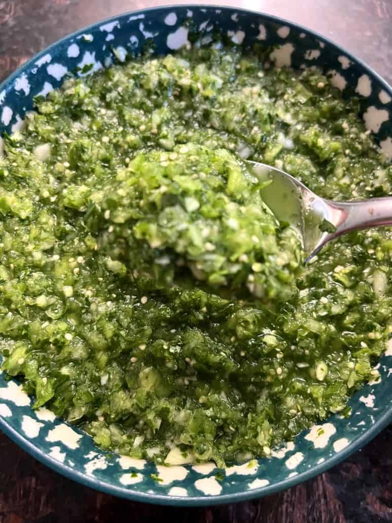 A spoon scooping up freshly made tomatillo salsa verde from a bowl.