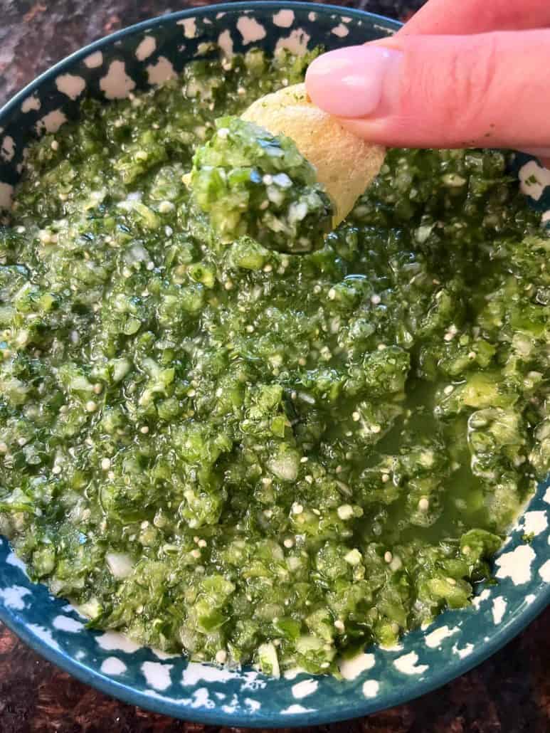 A hand dipping a tortilla chip into a bowl of fresh tomatillo salsa verde, perfect for snacking or as a topping for tacos and other Mexican dishes.