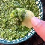 Close-up of a tortilla chip dipped in green raw tomatillo salsa verde.