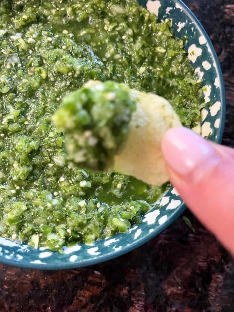 Close-up of a tortilla chip dipped in green raw tomatillo salsa verde.