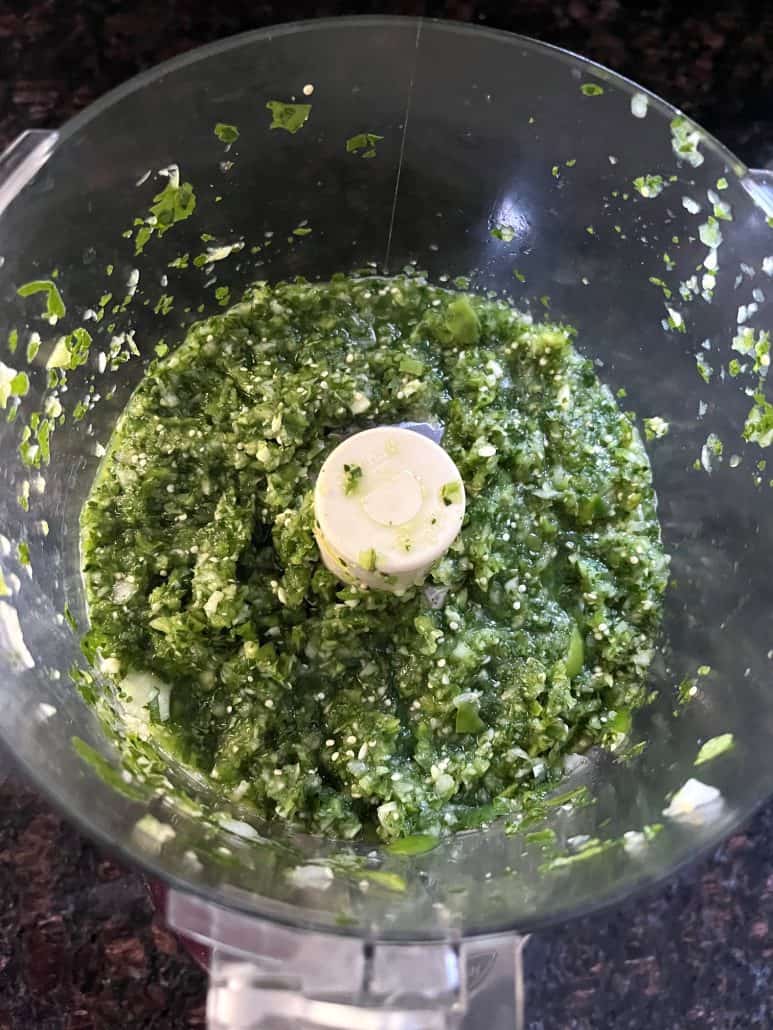 Top view of freshly blended tomatillo salsa verde in a food processor, highlighting the vibrant green color and textured consistency. 