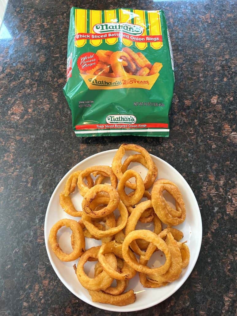 Plate of crispy golden onion rings served next to the Nathan’s Thick Sliced Battered Onion Rings package, ready to enjoy.