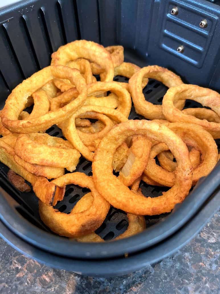 Side angle view of crispy, golden onion rings in an air fryer basket, highlighting their deliciously crunchy texture.