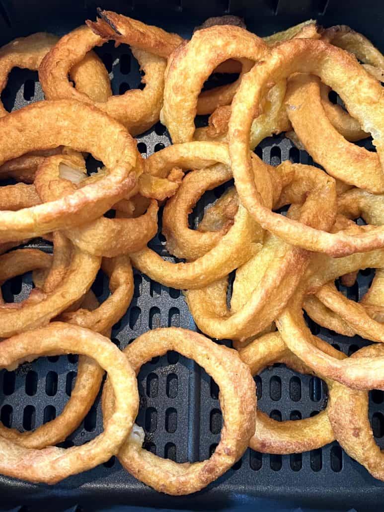 Close-up of perfectly crisped onion rings in an air fryer basket, showcasing their golden brown texture.