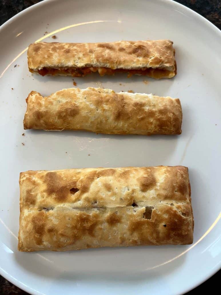 Three golden pizza sticks on a white plate, showcasing their crispy, flaky crusts.